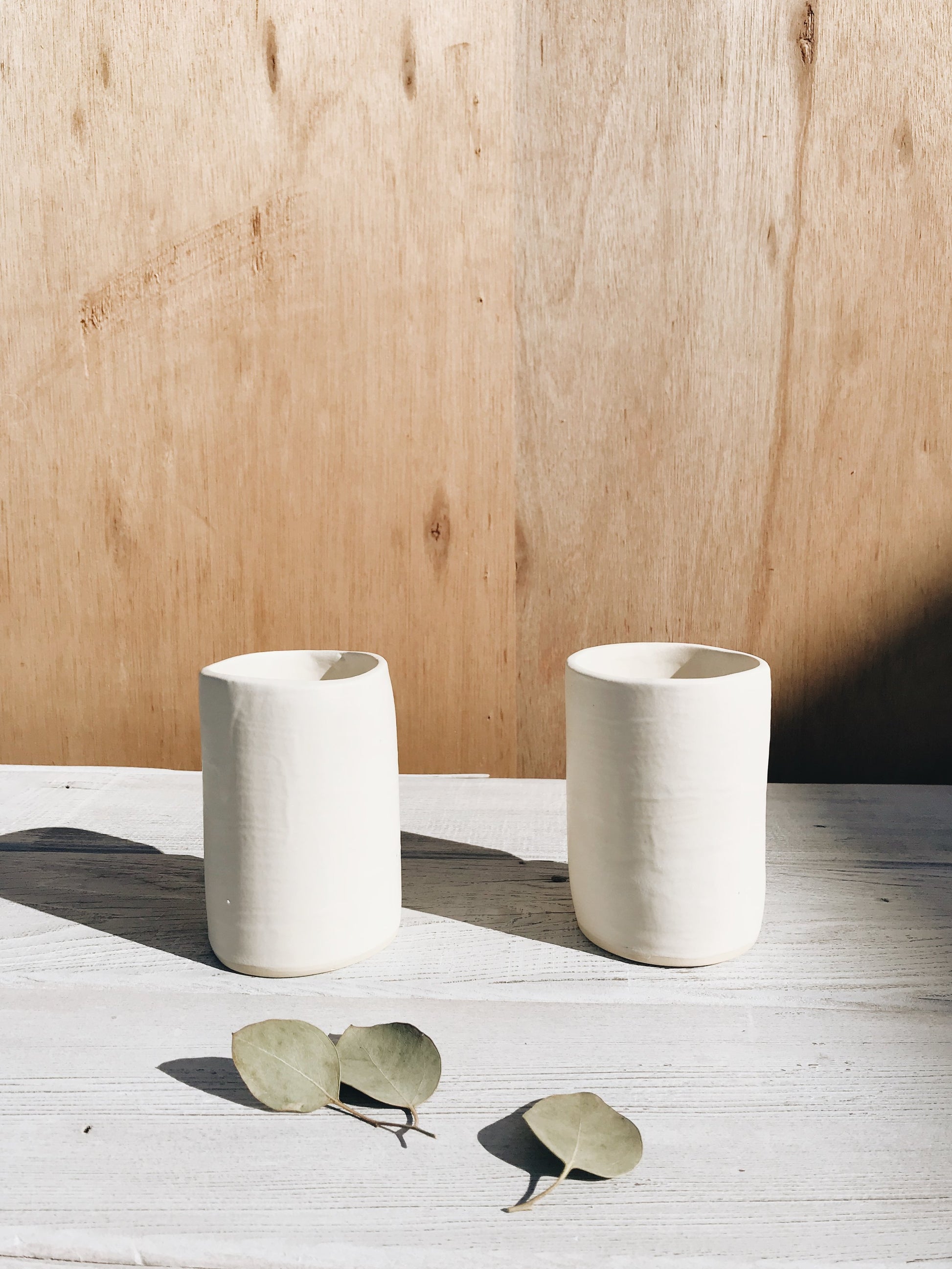 Two ceramic cups in matte white on wooden background.