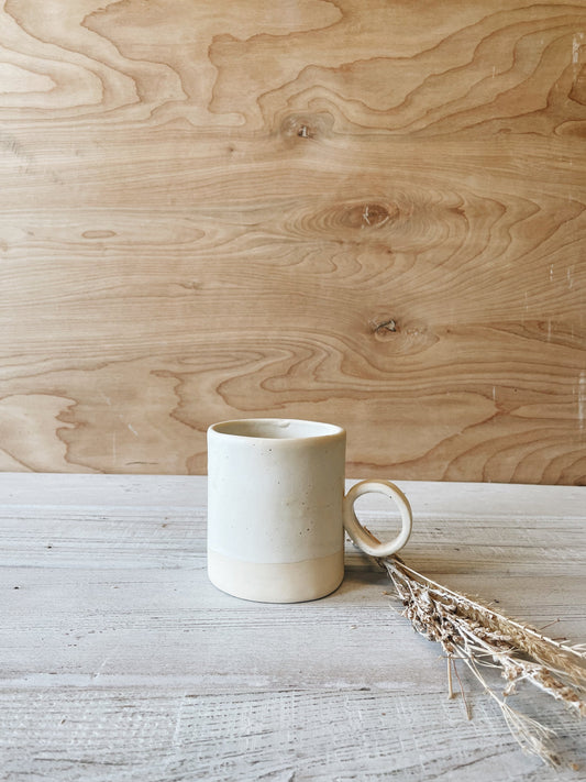 Circle handle ceramic mug in oatmeal on wood background.